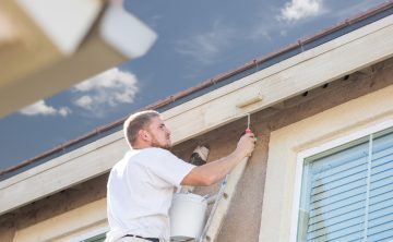 Professional Painter Using A Small Roller to Paint House Fascia.